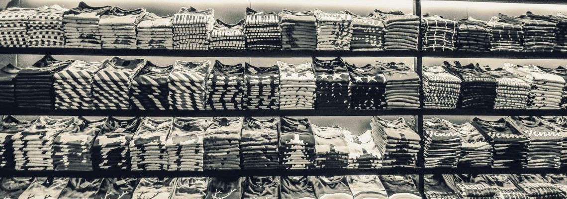 Black and white image showcasing neatly folded t-shirts stacked on store shelves.